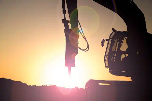 A hydraulic breaker arm at work during sunset.