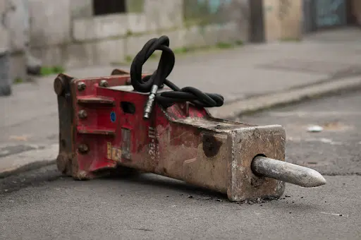 A hydraulic cement breaker lies on the ground at a job site.